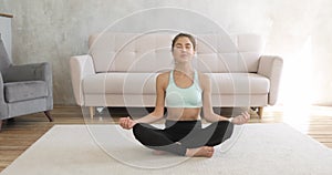 Young woman is making meditation after yoga practice at home sitting on carpet.