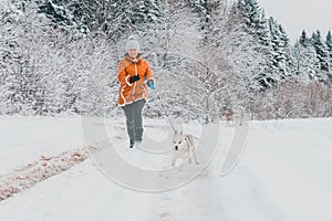 Young woman making a morning run with a husky puppy in the winter forest