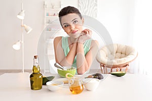 Young woman making nourishing mask with avocado in kitchen