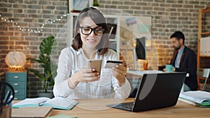 Young woman making online payment with credit card and smartphone at work