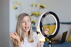 Young woman making photo or video content for social media with smartphone and light of ring lamp. Beauty blogger smiles