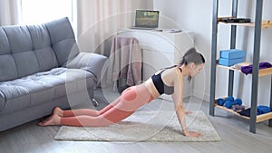 Young woman making push-ups exercise from knees at home on carpet, side view.