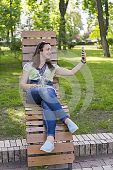 Young woman making selfie in the park. Sexy young woman with long blond hair doing selfie on summer day in park. vertical photo