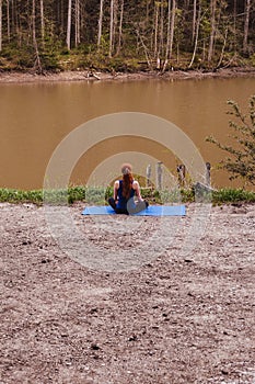 Young woman making yoga near river. Afar.