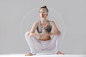 Young woman in Malasana pose, grey studio background