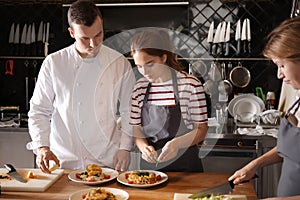 Young woman with male chef preparing tasty dish during cooking classes in restaurant kitchen