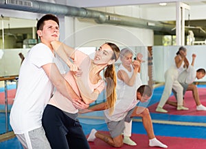 Young woman with male partner practicing basic elbow kick to chin during back grab