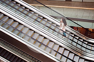 Young woman at the Mall rise up by escalator, view from the top