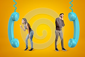 Young woman and man in casual outfits, each standing near one of two big blue landline phone receivers on yellow