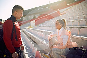 Young woman and man are chatting on the grandstand after a training at the stadium. Sport, athletics, athletes