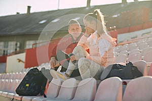 Young woman and man are chatting while sitting on the grandstand after a training at the stadium. Sport, athletics, athletes