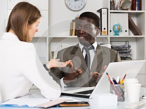 Young woman and man colleagues working at laptop and discussing