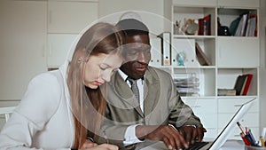 Young woman and man colleagues working at laptop and discussing in office