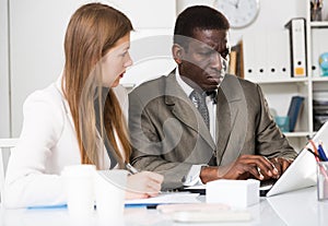 Young woman and man colleagues working with laptop and papers