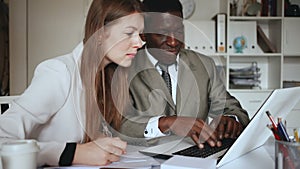 Young woman and man colleagues working with laptop and papers in office