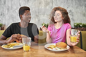 Young woman and man eating hamburgers, french fries in cafe.