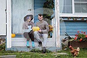 Young woman and man, family, sitting on porch of village house with pumpkins.