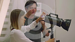 Young woman and man get ready light device for photoshoot