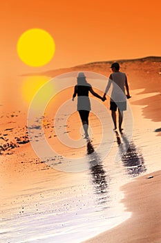 Young woman and man in love walking hand in hand on beach with beautiful sunset