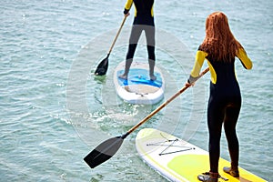 Young woman and man paddling on SUP board at sea at sunny day