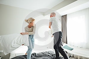 Young woman and man play and fight on pillows while sitting at apartment