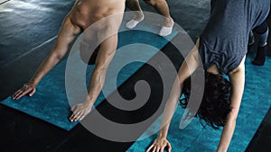 Young woman and man practicing yoga with downward dog pose on the gym floor. Two people couple working out indoors.