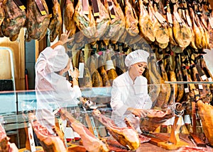 Young woman and man selling ham in jamoneria