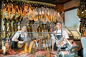 Young woman and man selling ham in jamoneria