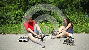 Young woman and man sitting on track, putting their rollerblades on their feet.