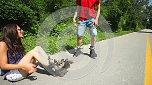 Young woman and man sitting on track, putting their rollerblades on their feet.