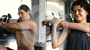 Young woman and man stretching their arms on the gym floor. Two people couple working out indoors.