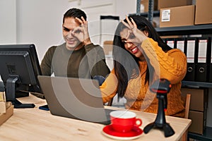 Young woman and man working at small business ecommerce smiling happy doing ok sign with hand on eye looking through fingers