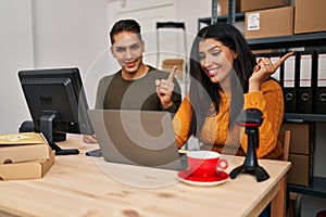 Young woman and man working at small business ecommerce smiling happy pointing with hand and finger to the side