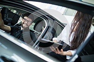 Young woman Manager showing something on a clipboard to the customer in car showroom