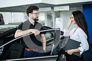 Young woman Manager showing something on a clipboard to the customer in car showroom