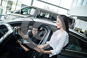 Young woman Manager showing something on a clipboard to the customer in car showroom