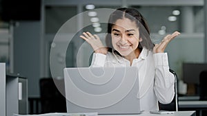 Young woman manager sitting in office looking at laptop screen receiving notification reads good news rejoices in