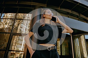 Young woman manager is talking mobile phone whiile standing on modern building background