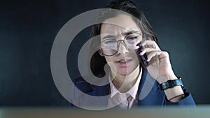 Young woman manager talking by mobile phone working on laptop in business office. Business woman using mobile for