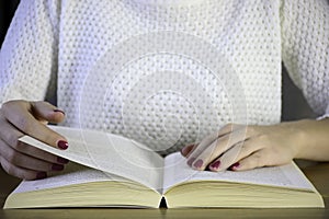 Young woman with manicure sitting at the table and reading book