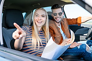 young woman with map in hand pointing by finger to smiling boyfriend