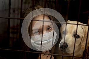 Young woman in mask behind girds or bars with her dog. forced home isolation