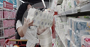 Young woman in a mask from a coronavirus epidemic buys toilet paper in a supermarket, where people panicky buy