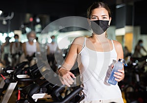 Young woman in mask with fitness bike in gym