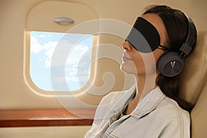 Young woman with mask resting while listening to music in airplane during flight