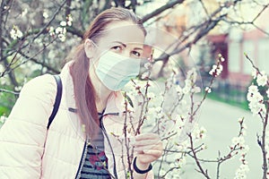 Young woman in a mask stands near a flowering tree