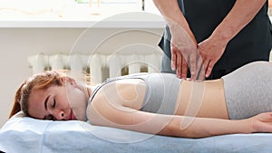 Young woman at massage session - lying on a couch - the massagist pressing on her spine with his fingers