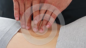 Young woman at massage session - the massagist pressing on her spine with his fingers