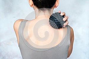Young woman massages her back with spiky trigger point ball, muscle pain treatment reflexology. Physiotherapy concept