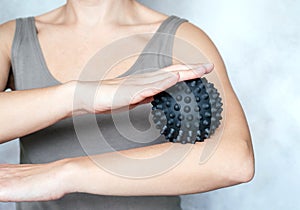 A young woman massages her elbow with spiky trigger point ball, tennis elbow exercises
